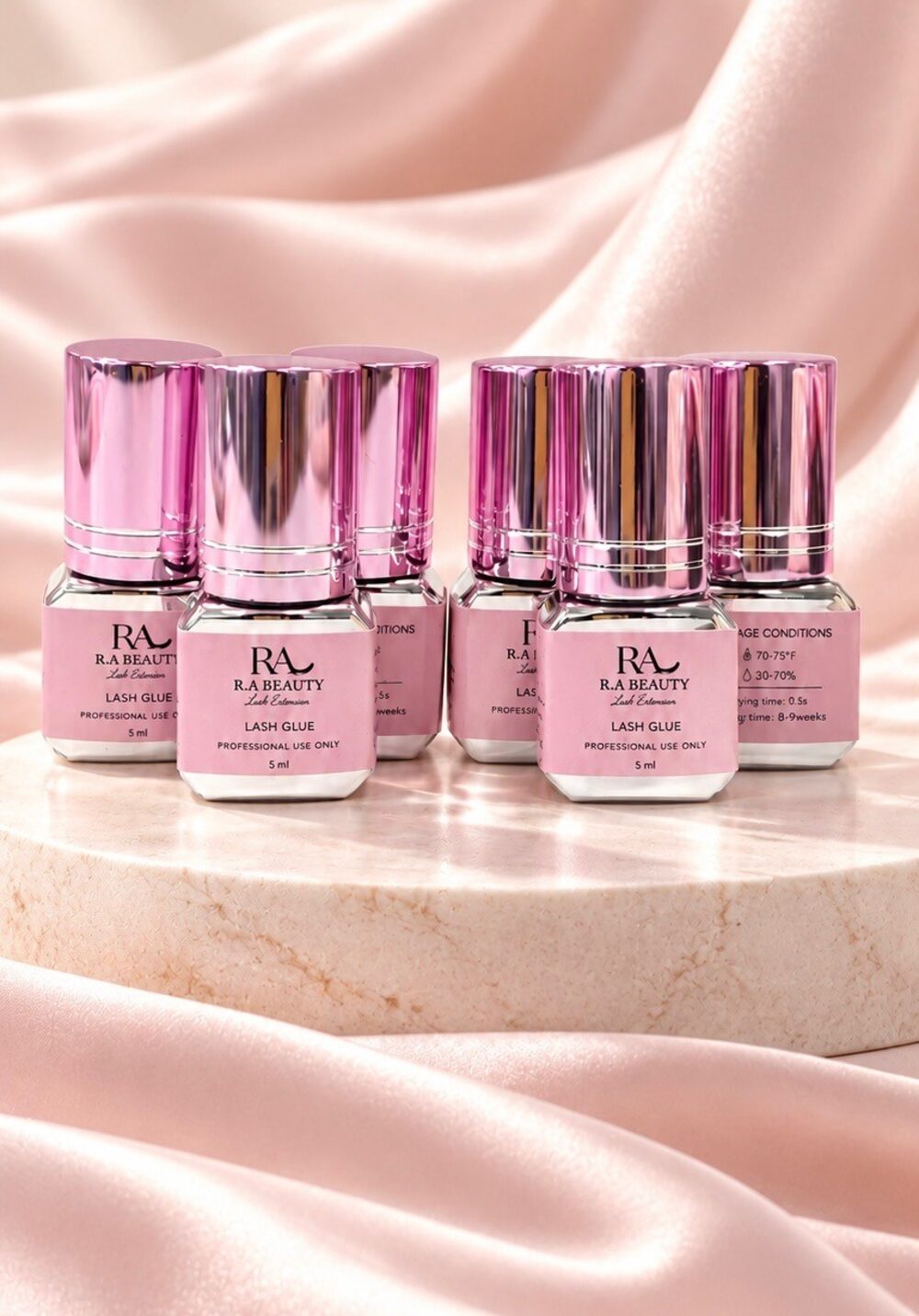 A collection of R.A Beauty Lash Glue bottles with pink metallic caps